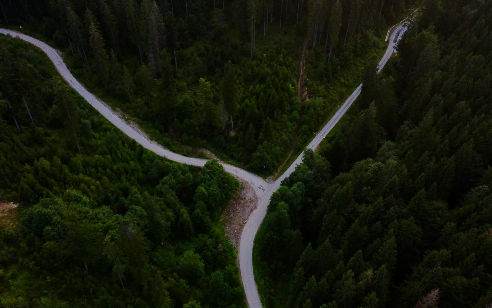 An aerial view of a Y-shaped road junction where two winding roads merge through dense green forest