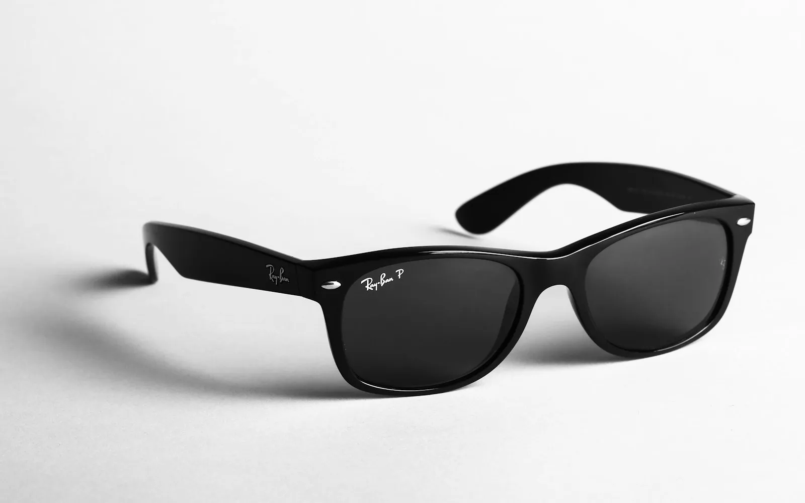 A pair of black Ray-Ban Wayfarer sunglasses with polarised lenses on a white surface