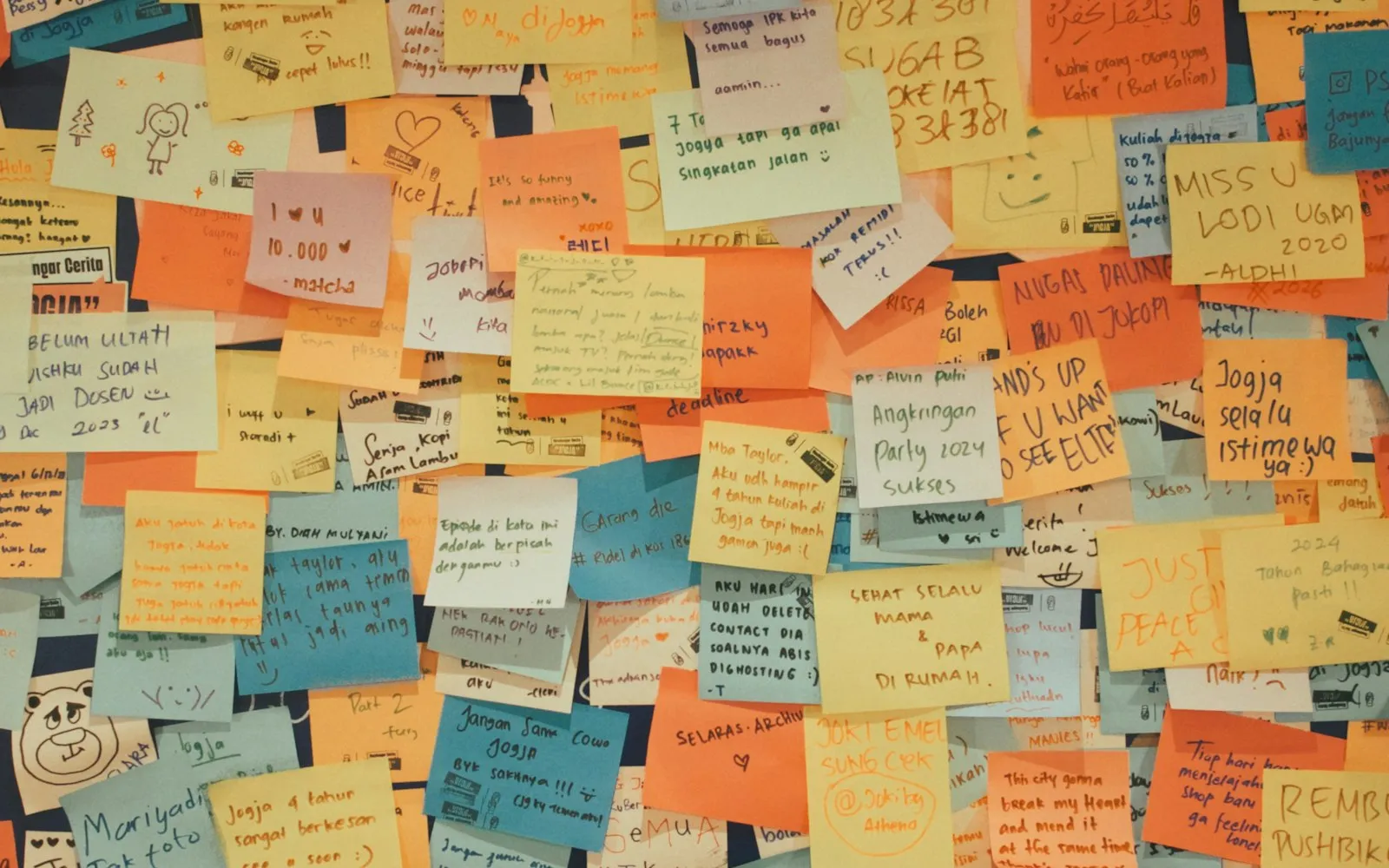 A bulletin board covered in overlapping handwritten sticky notes in orange, yellow, blue and white