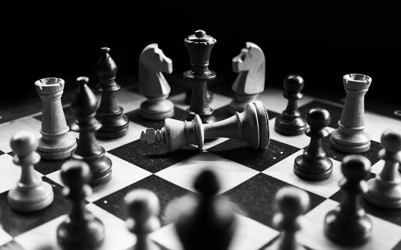 A black-and-white photo of a chess board mid-game, with a king piece knocked over among the other pieces