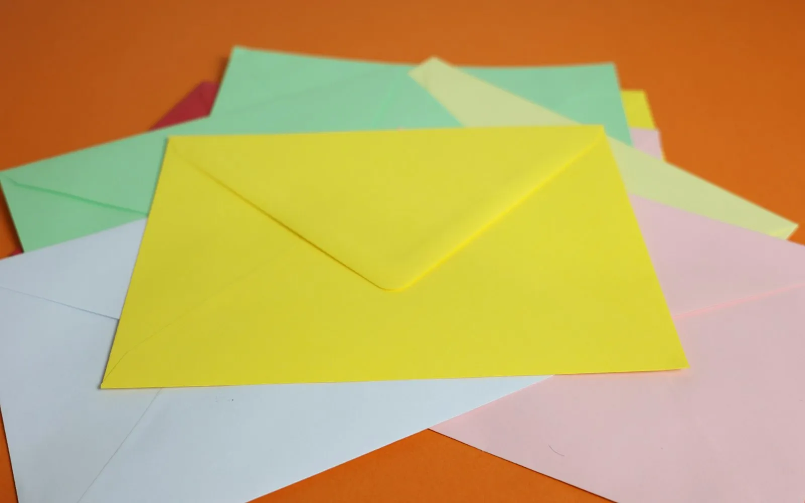 A pile of colourful envelopes in yellow, green, pink and white on an orange background