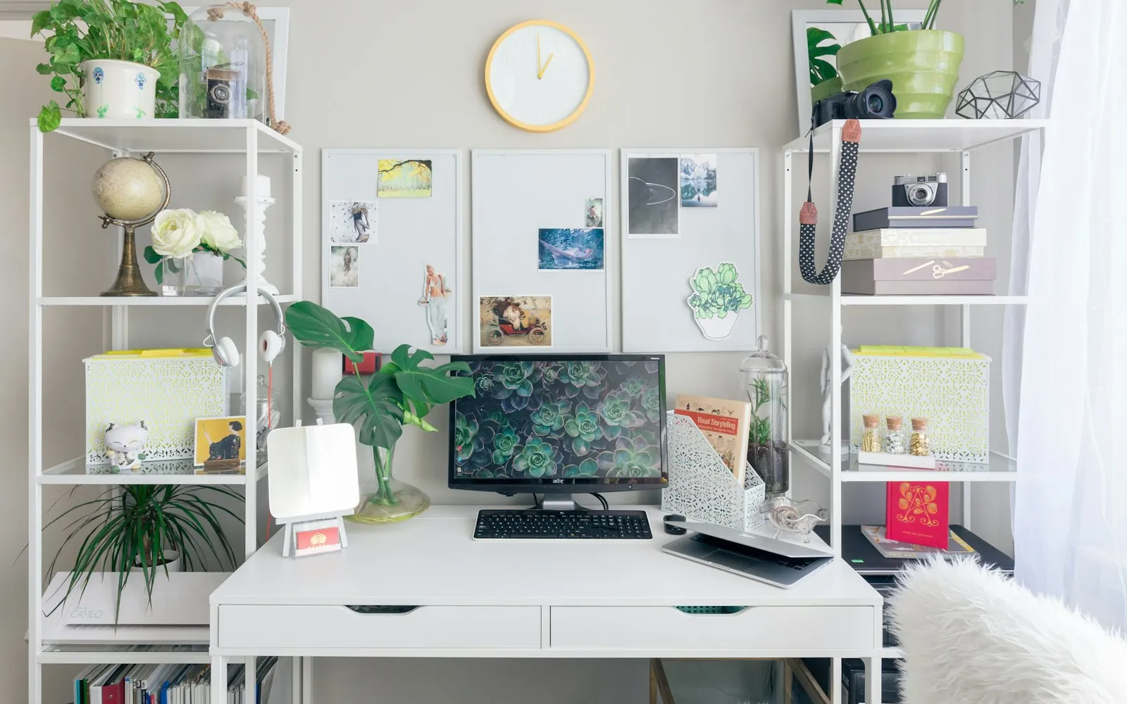 A bright home office with a white desk, a monitor, plants and white shelves