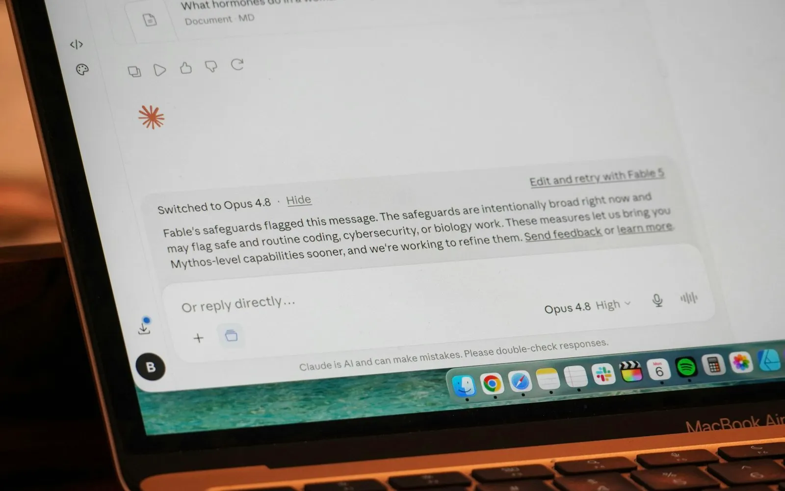 A MacBook Air showing a Claude chat with a notice that the reply switched to Opus 4.8, above the message box and the macOS dock
