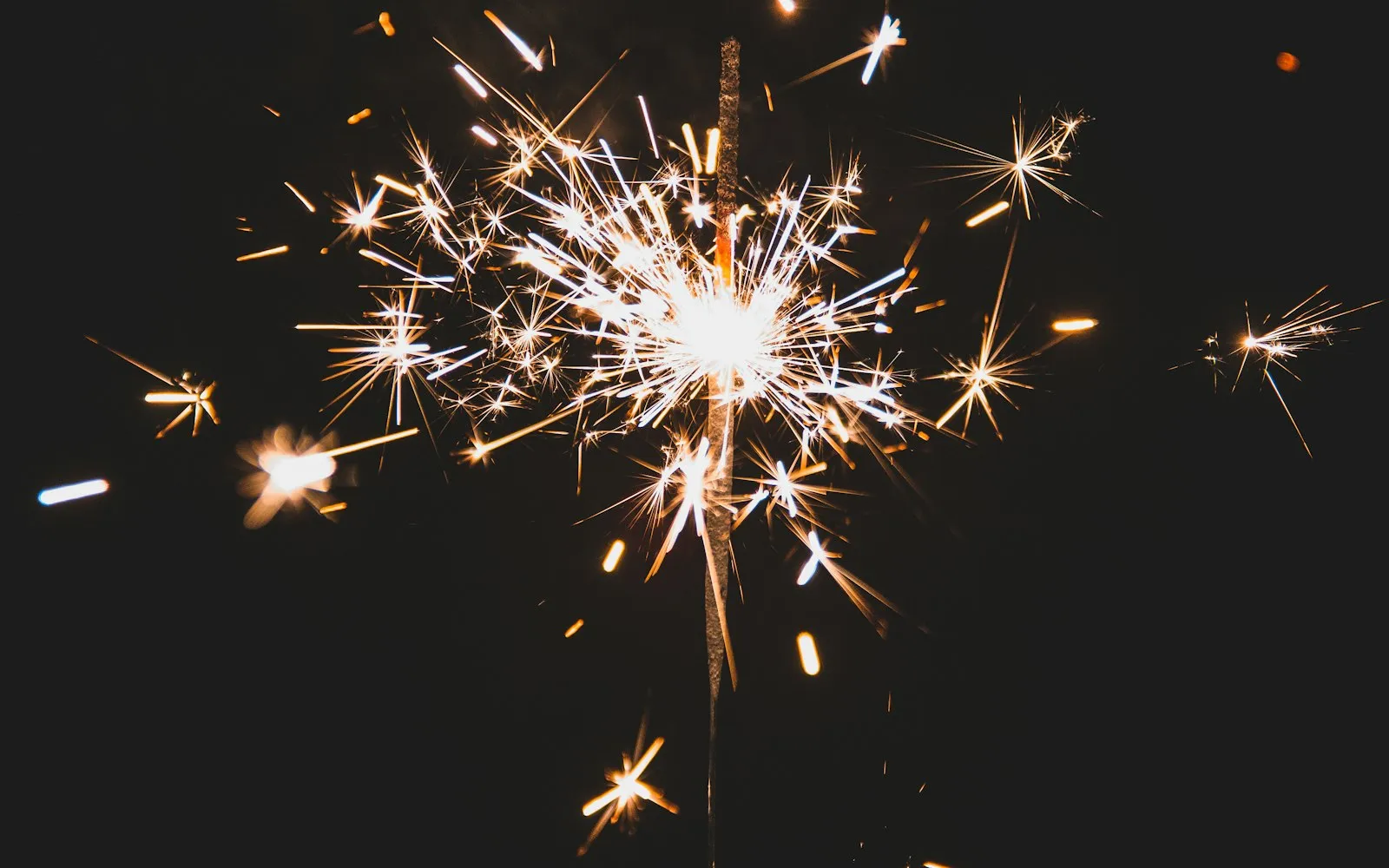 A lit sparkler throwing bright sparks against a black night sky