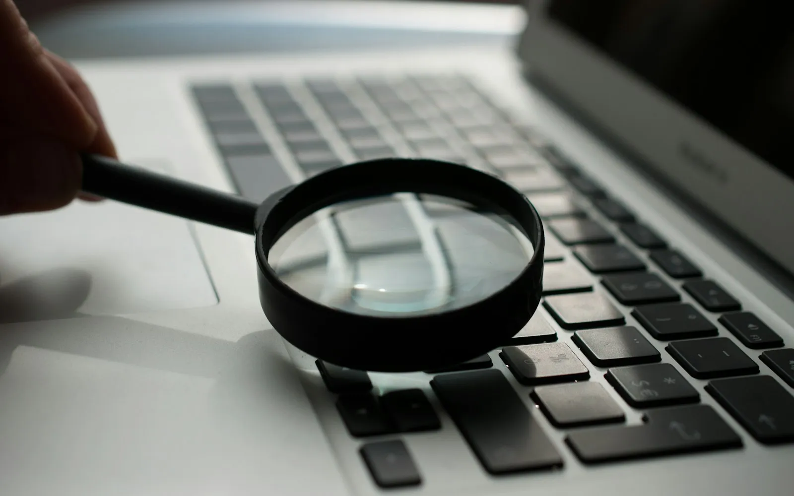 A magnifying glass held over the keyboard of a grey laptop