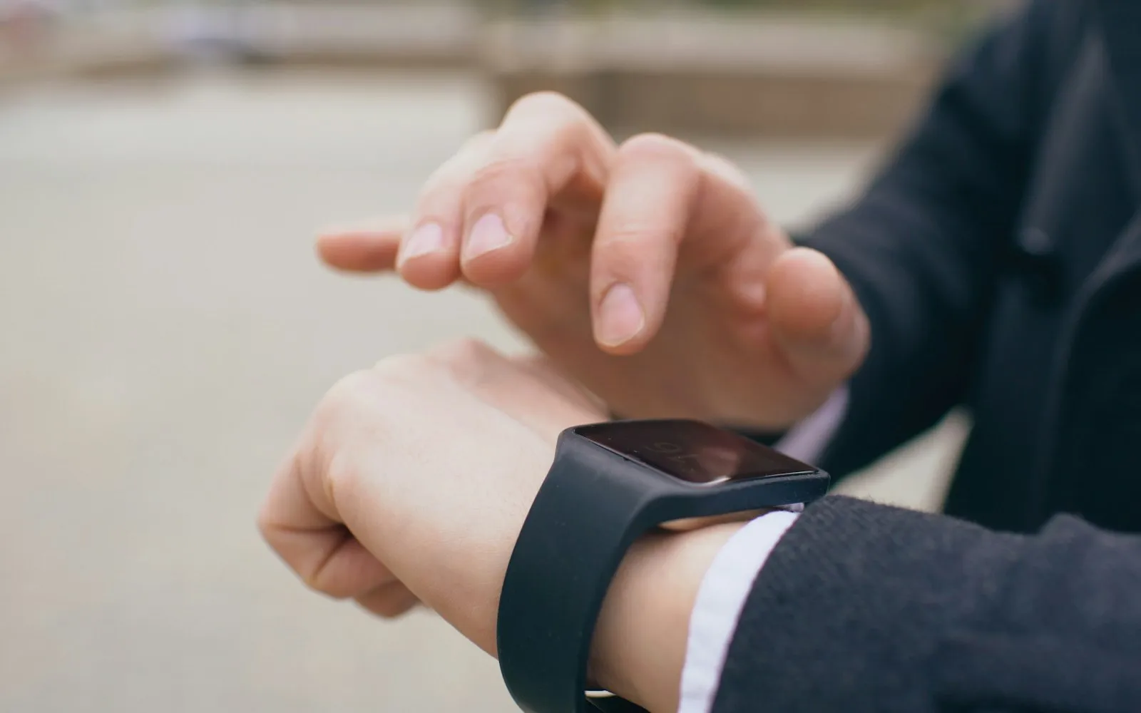 A man in a dark jacket touching a black smartwatch on his wrist with his other hand