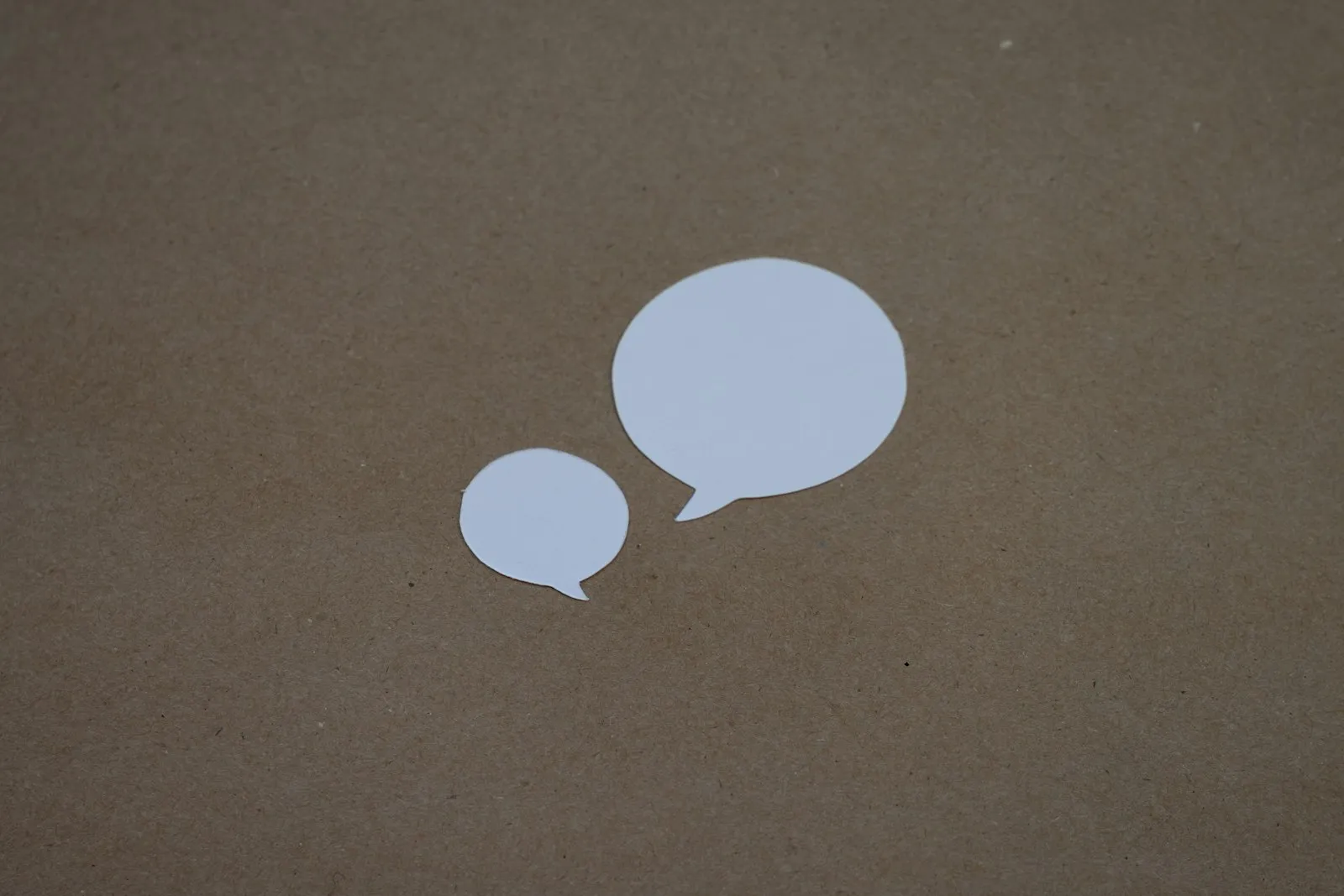 Two white paper speech bubbles cut out and laid on brown paper