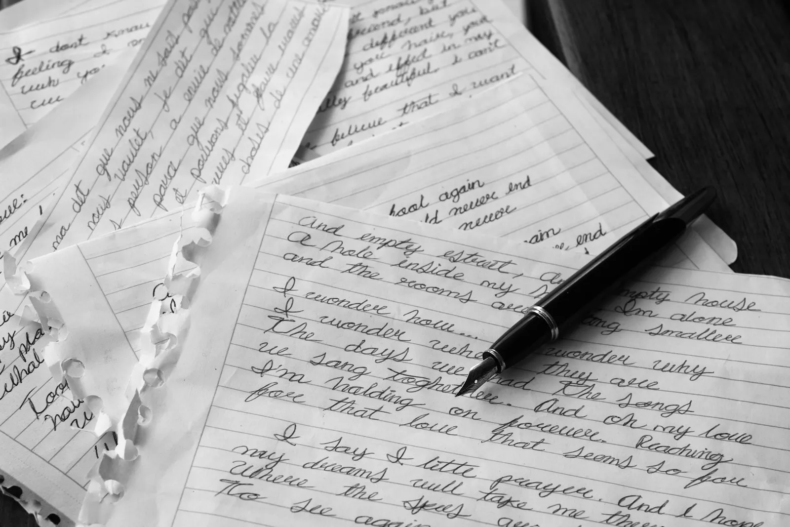 A black pen resting on loose handwritten pages, in black and white
