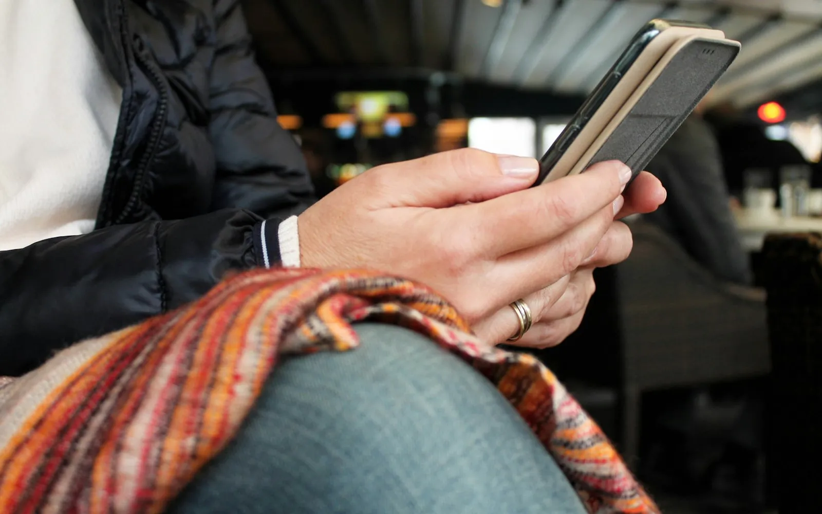 A person sitting in a café holding a smartphone, with a colourful striped scarf across their lap