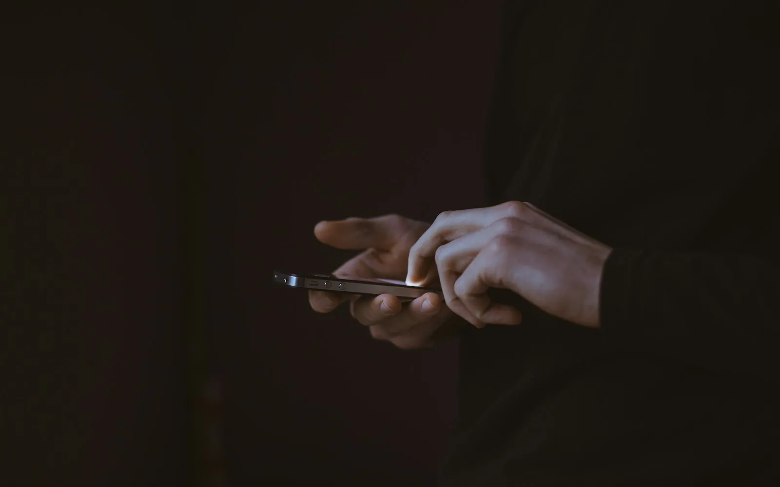 Two hands holding a smartphone against a dark background