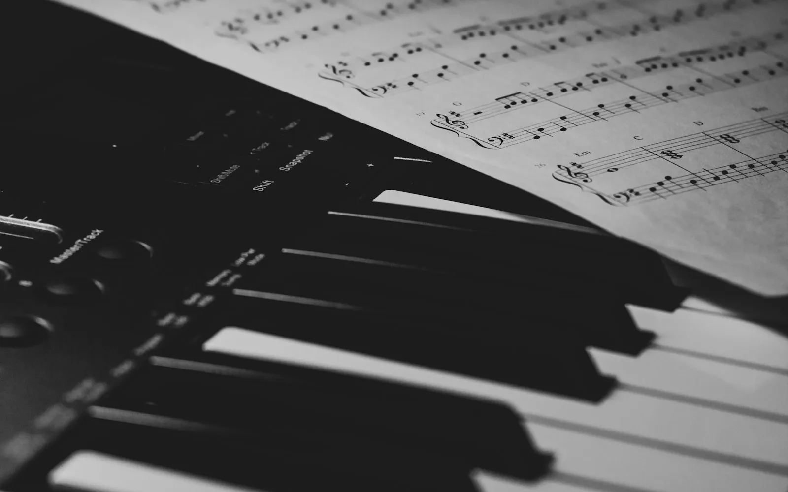 A black-and-white close-up of piano keys with a sheet of printed music resting on the keyboard