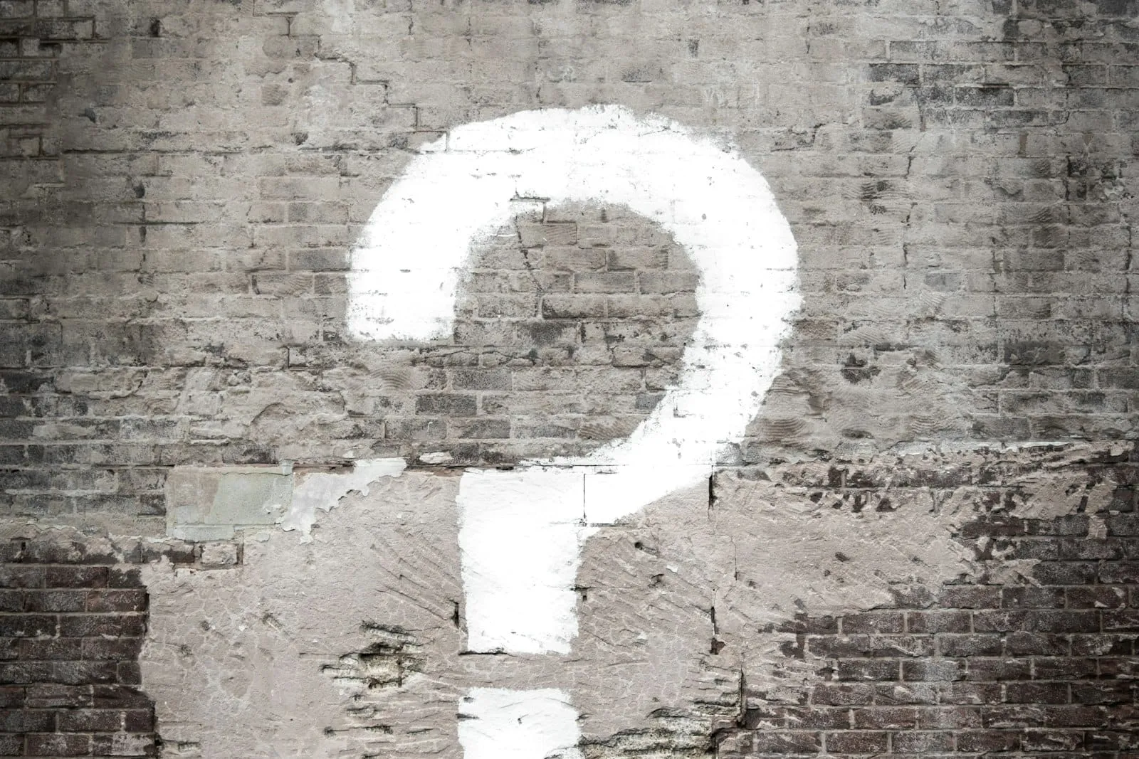 A large white question mark painted on a weathered brick wall