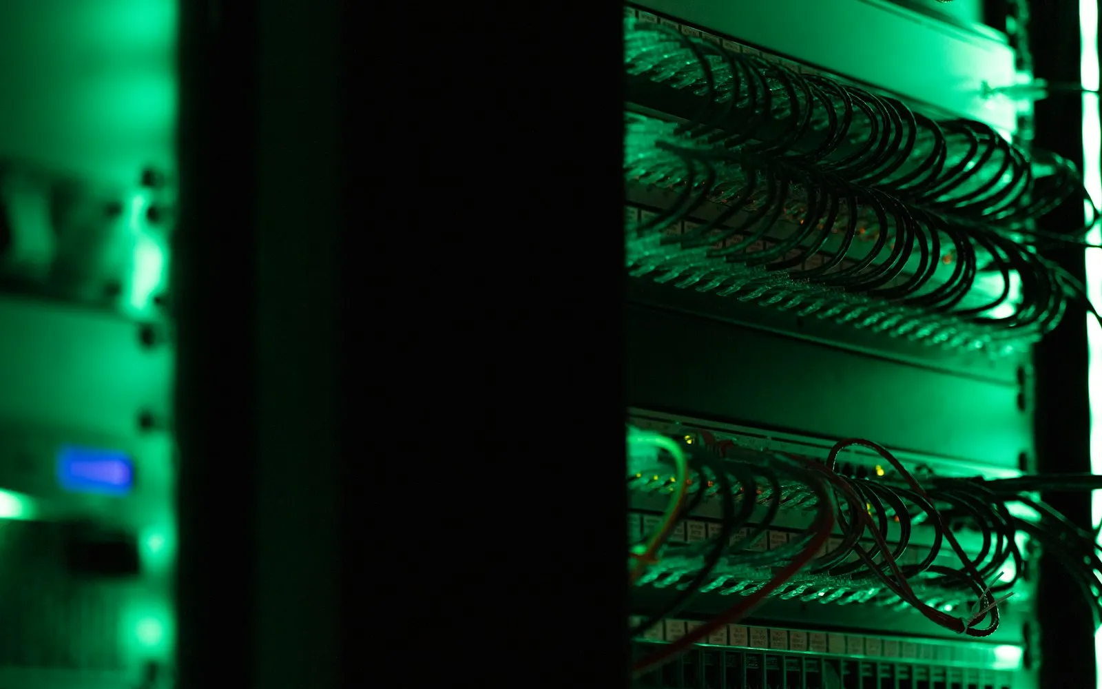 A dark server rack with neatly looped network cables lit by green light