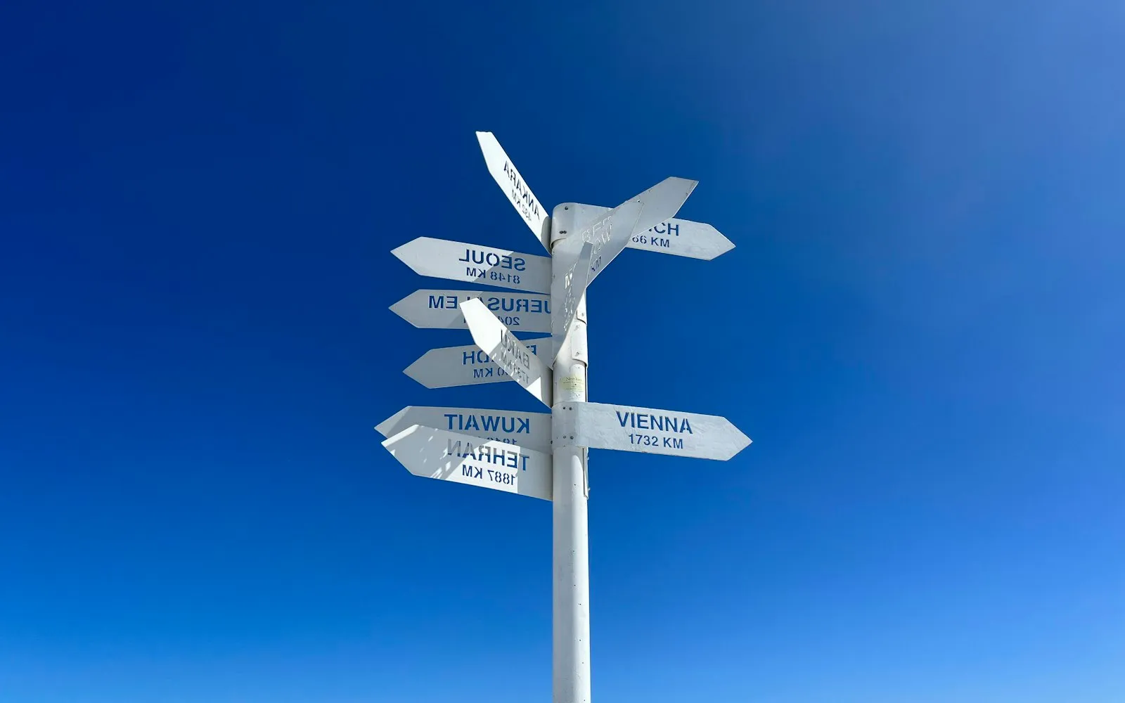 A white signpost with arrows pointing to different cities against a deep blue sky
