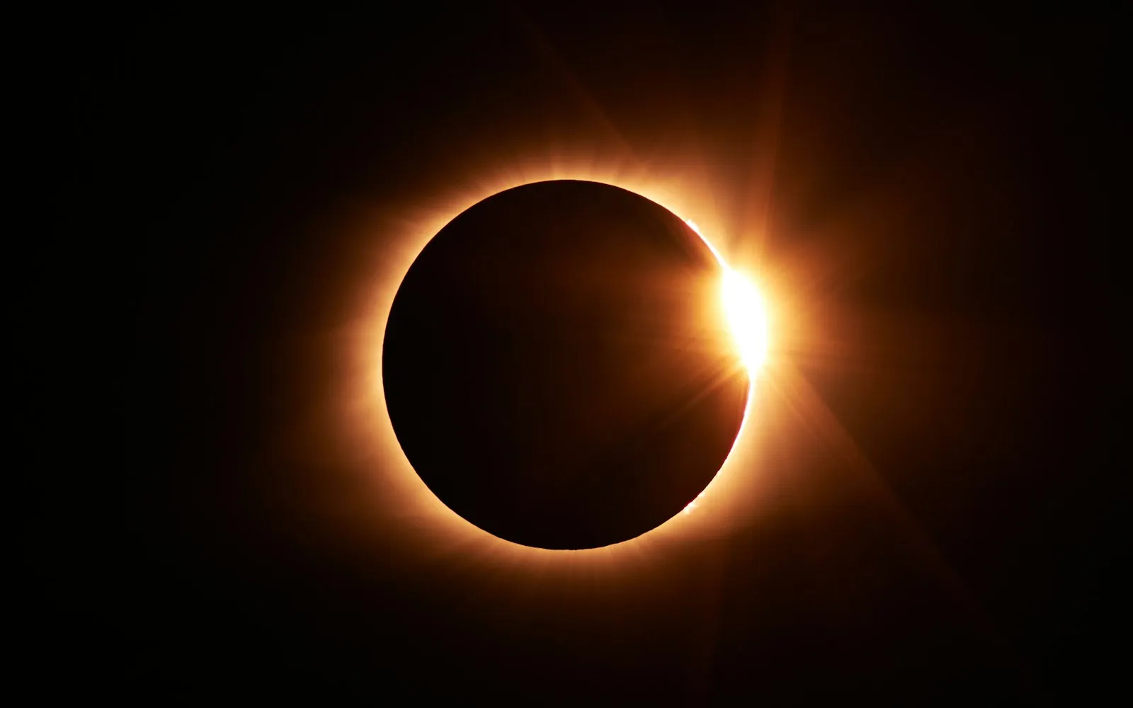 A total solar eclipse at the diamond ring moment, with the dark disc of the moon ringed by a glowing corona