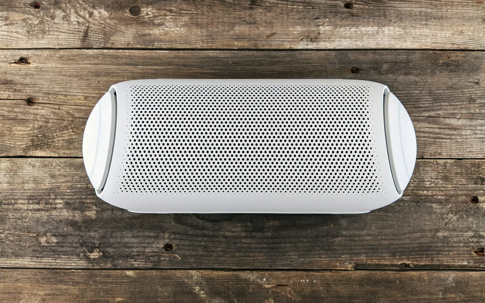 A white smart speaker with a perforated grille, seen from above on a weathered wooden floor